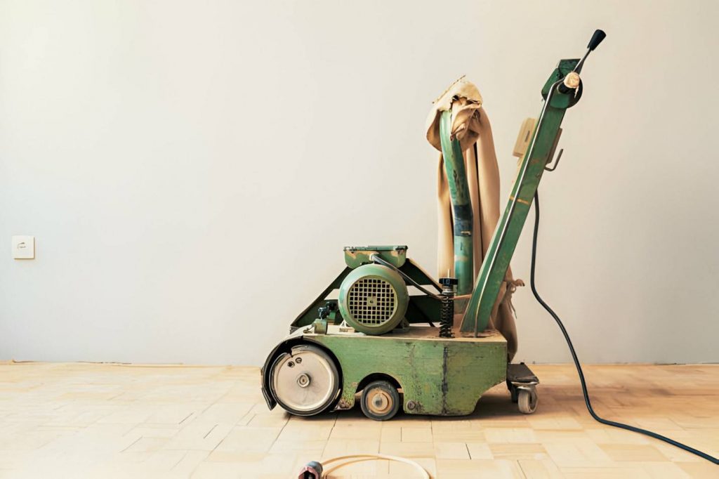 Closeup side view of an unrecognizable handyman using a sanding machine to remove the surface layer of a solid oak hardwood floor in a spacious living room.
