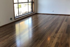Photo of an empty room with dark wood shinny flooring with window view